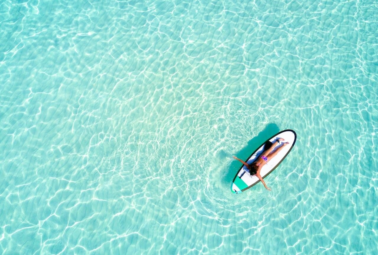 aerial-view-of-a-woman-on-a-surfboard-in-the-turquoise-waters-of-the-maldives.jpg